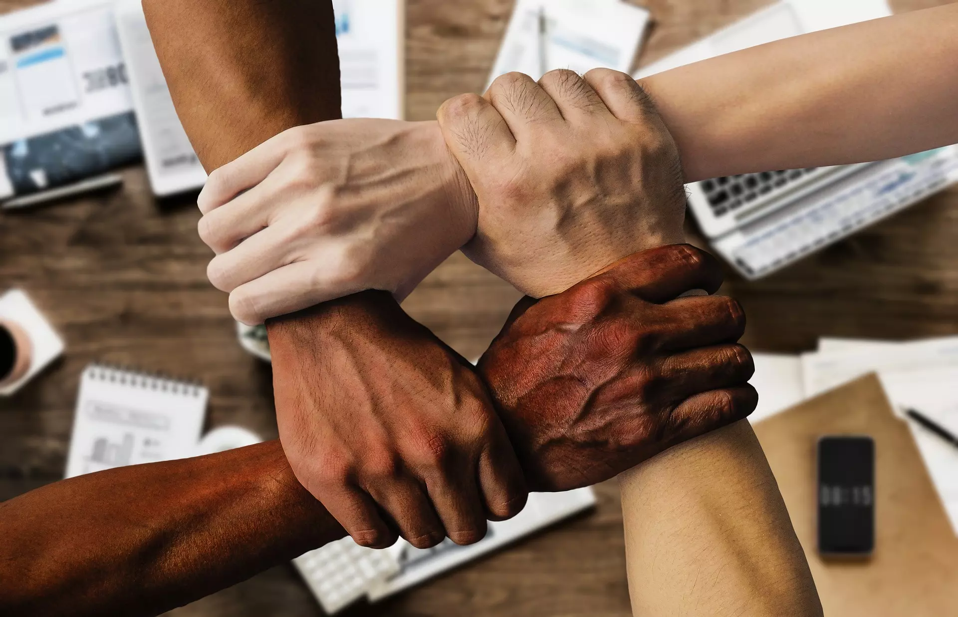 Four hands grasping each other by their wrists to create an interlocking pattern